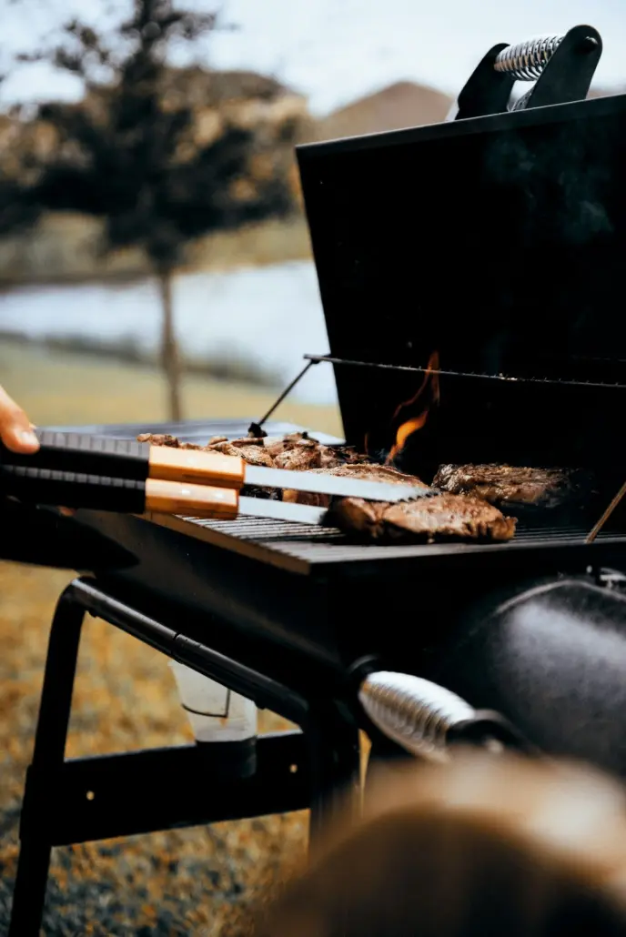 person using tongs to flip meat on a hot grill
