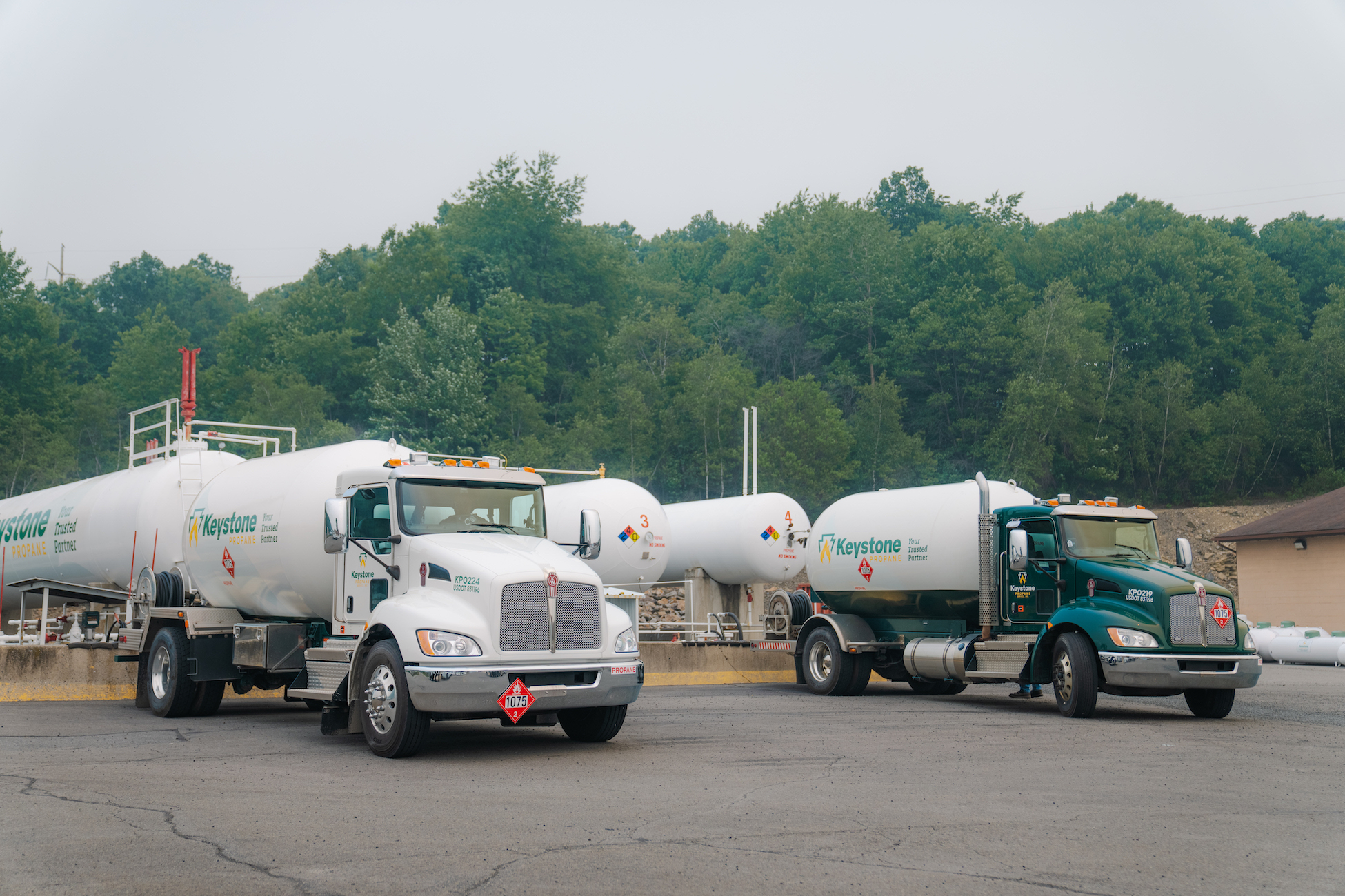 2 Propane trucks parked in front of large storage tanks
