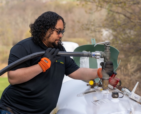 Employee filling propane tank using hose from delivery truck