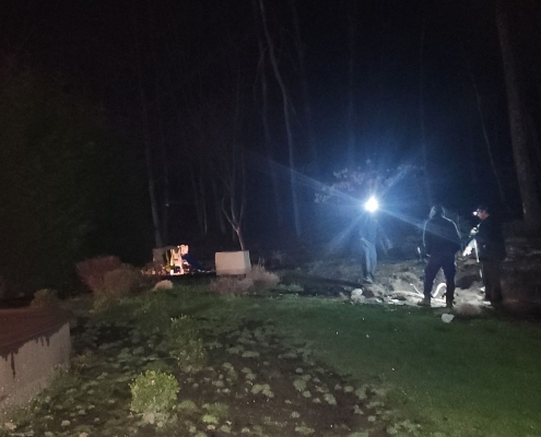 Wide shot of 3 employees at night looking over hole in yard